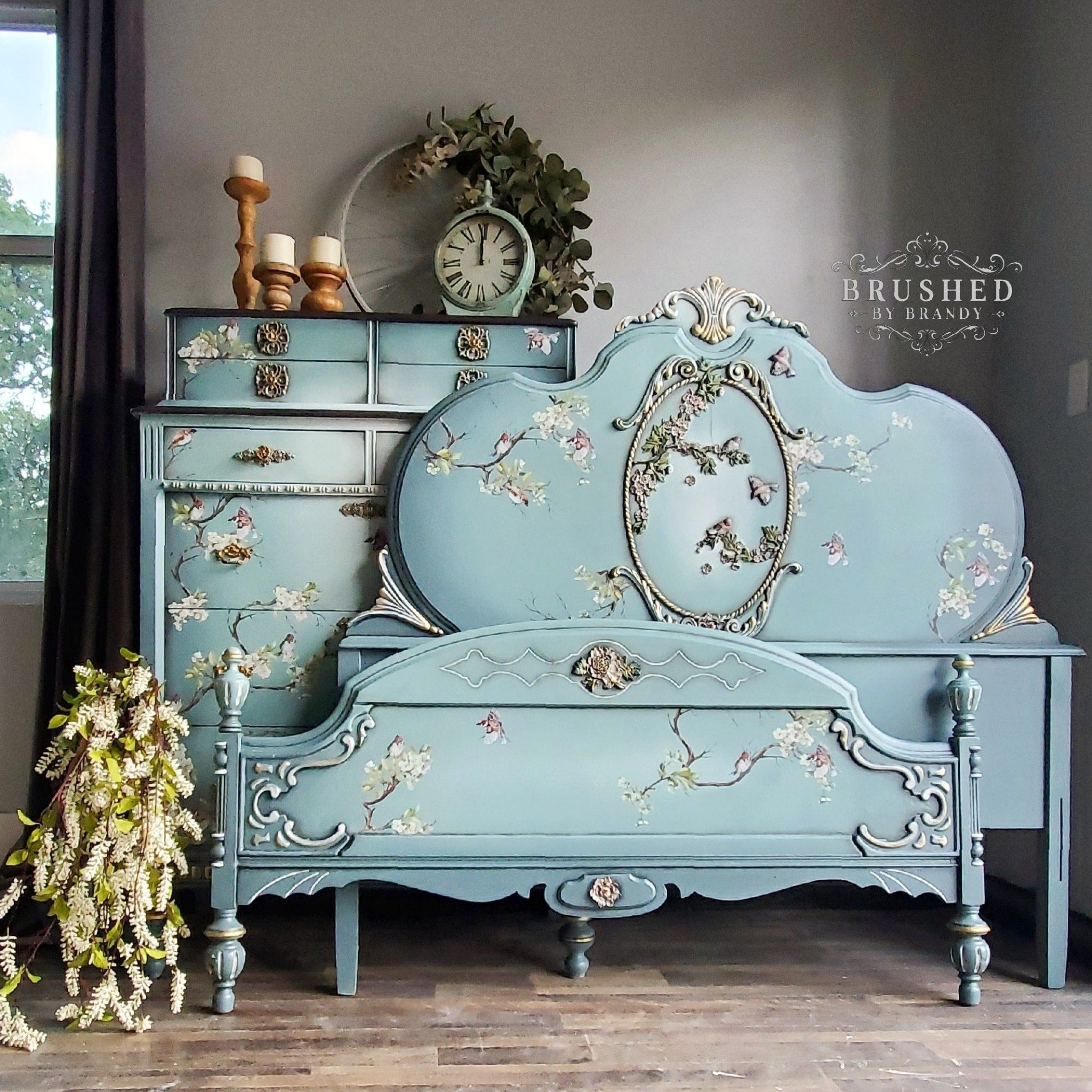 A vintage bedroom furniture set containing a headboard, footboard, and chest dresser refurbished by Brushed by Brandy are painted light blue and feature ReDesign with Prima's Blossom Flight transfer on them.