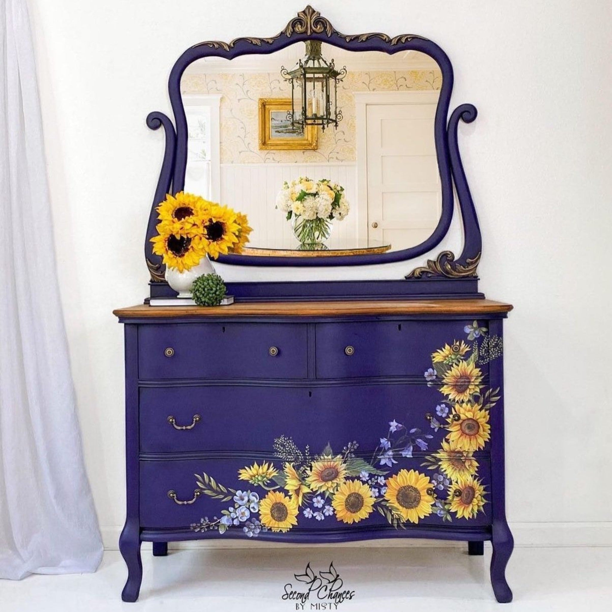 A vintage dresser with an attached mirror refurbished by Second Chances by Misty is painted Navy blue and features ReDesign with Prima's Sunflower Fields transfer along the front bottom and up the front right side of the drawers.