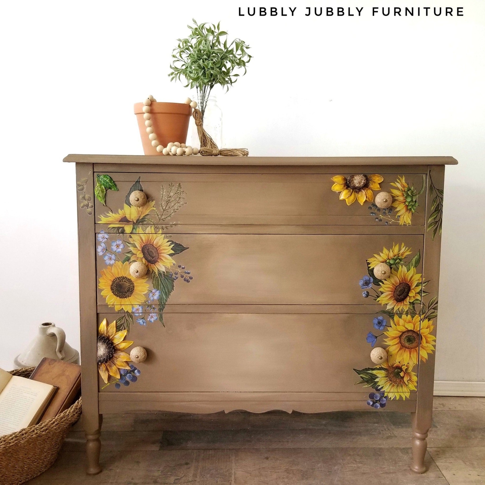 A vintage 3-drawer dresser refurbished by Lubbly Jubbly Furniture is painted a blend of light and medium brown and features ReDesign with Prima's Sunflower Fields on the left and right side of the front of its drawers.