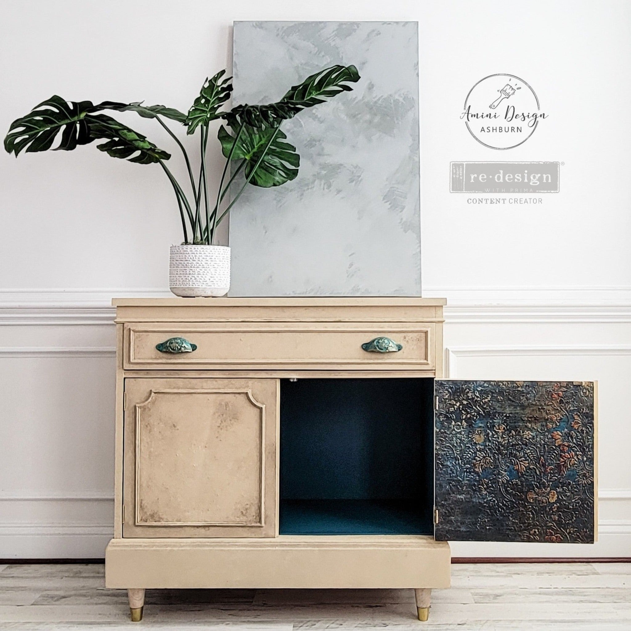 A vintage small console table refurbished by Amini Deisgn Ashburn is painted beige and features ReDesign with Prima's Aged Patina A1 fiber paper inside its doors.