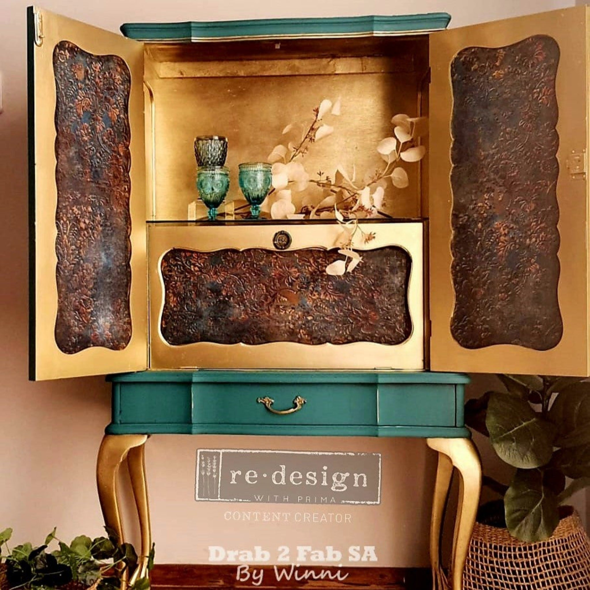 A vintage small armoire refurbished by Drab 2 Fab SA by Winni is painted a soft teal green with gold accents. Inside its 2 doors is painted gold and features ReDesign with Prima's Aged Patina A1 Fiber paper in the door inlays and on a drawer.