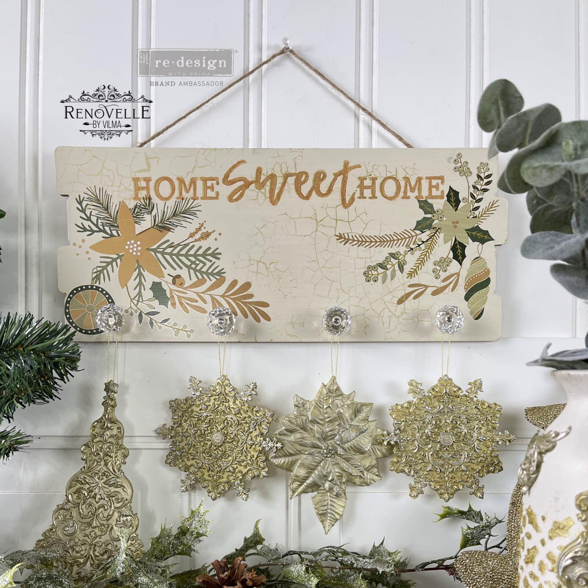 A wood hanging sign created by Renovelle by Vilma is painted a crackle beige and features ReDesign with Prima's Holiday Spirit small transfer on it. At the top of the sign it reads: Home Sweet Home and crystal knobs for hanging decorations are at the bottom.