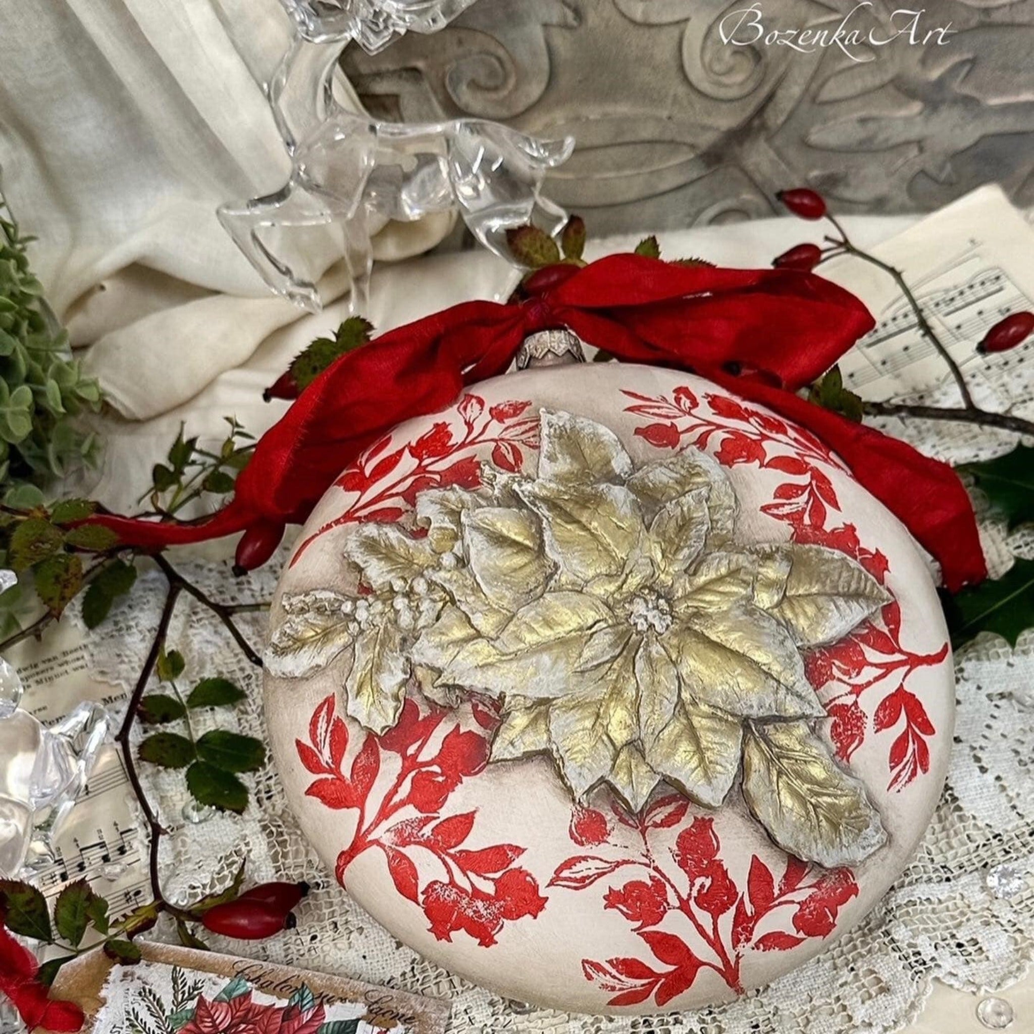 An ornament created by Bozenka Art is painted beige with a red leafy stamp design and has a gold and white silicone mould casting of ReDesign with Prima's Perfect Poinsettia.