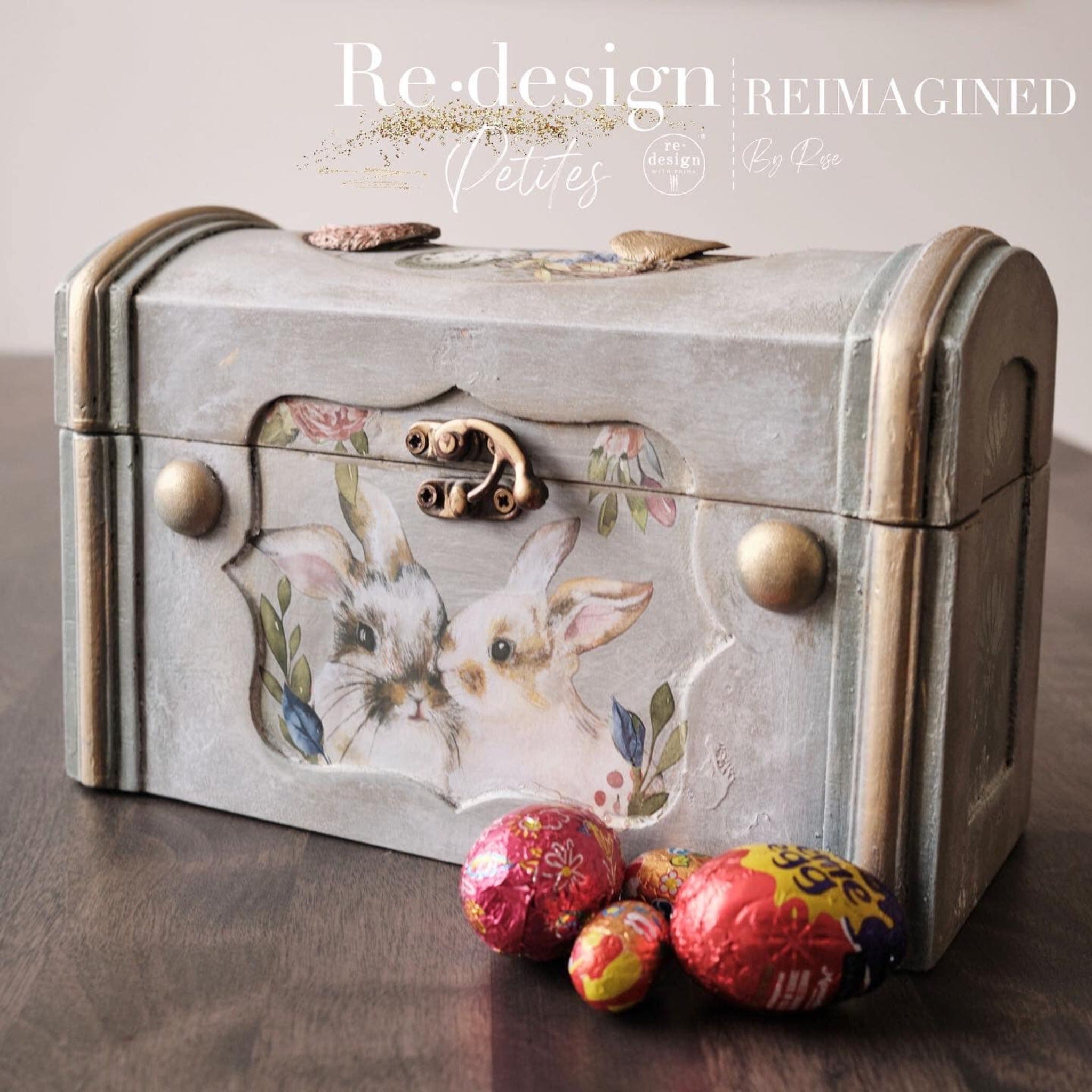 A vintage small wood box refurbished by Reimagined by Rose is painted light grey with gold accents and features ReDesign with Prima's Cottontail small transfer on its front inlay.