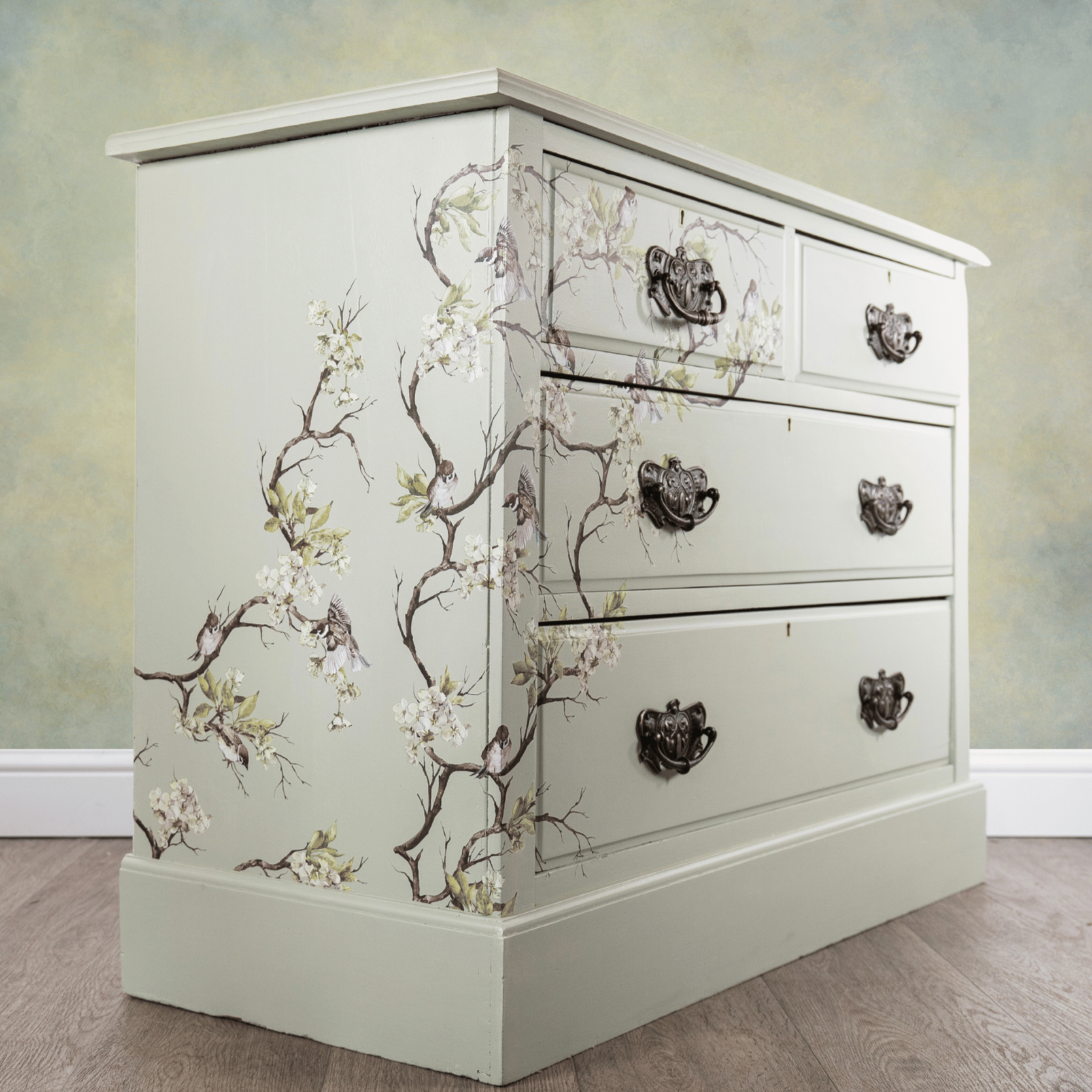 A corner angle view of a small 4-drawer dresser is painted soft white and features ReDesign with Prima's Blossom Flight transfer on it.