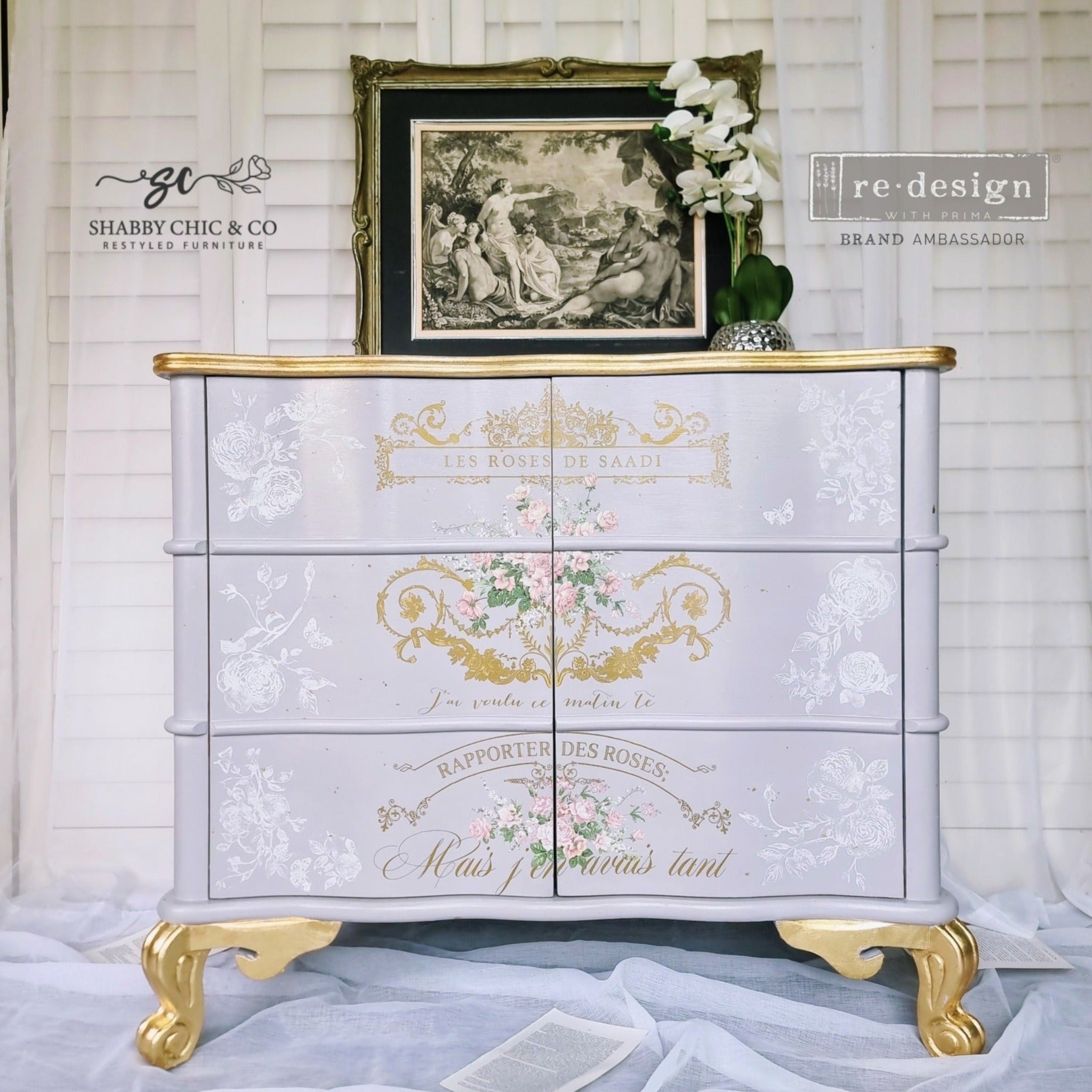 A vintage 6 drawer dresser refurbished by Shabby Chic & Co. is painted light grey with gold accents and features ReDesign with Prima's Kacha Les Roses transfer down the center of the dresser.