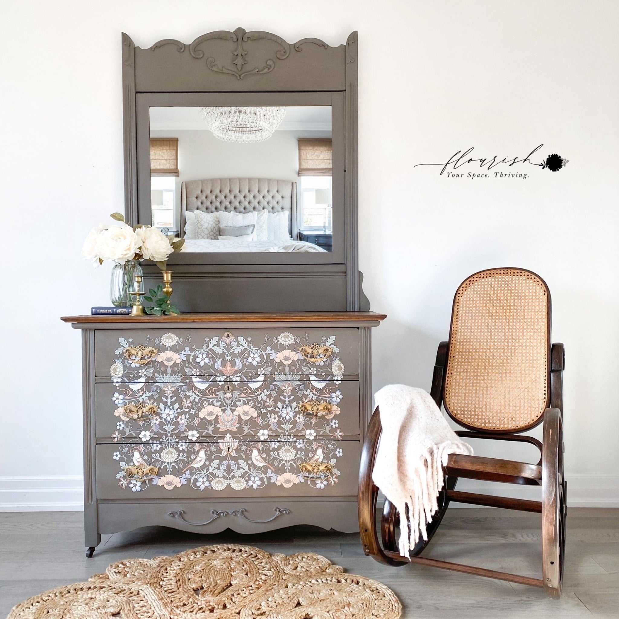 A vintage 3-drawer dresser with an attached mirror refurbished by Flourish Your Space Thriving is painted a light grey-brown and features ReDesign with Prima's Albery transfer on its drawers.