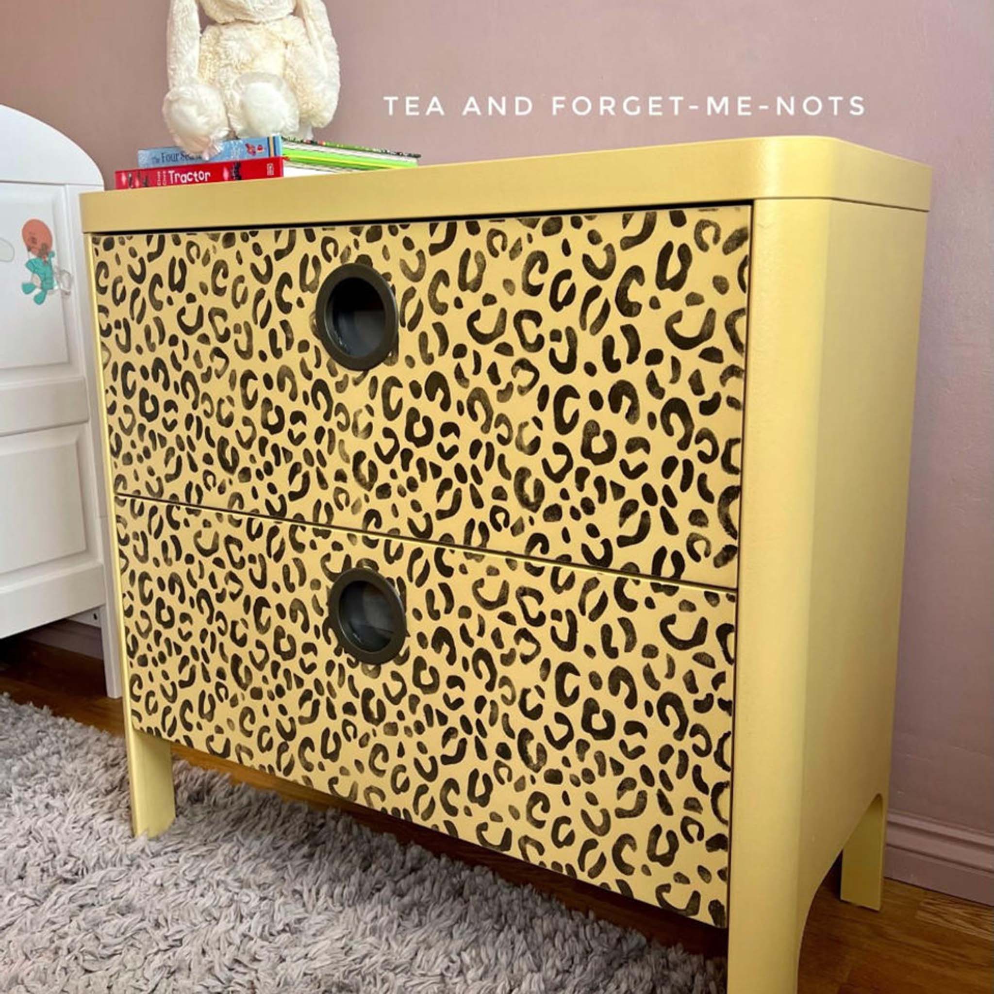 A 2-drawer small dresser refurbished by Tea and Forget-Me-Nots is painted pale yellow and features the cheetah print in black of Belles & Whistles Safari mylar stencil on the drawers.