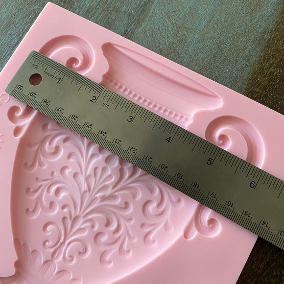 Pink silicone mold with intricate designs and a ruler for scale on a wooden surface.