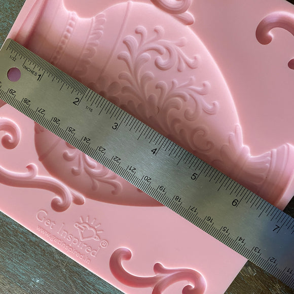 Pink decorative silicone mold with intricate patterns and a ruler for scale on a wooden surface.