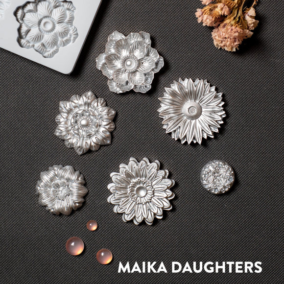 Silver colored silicone mold castings of 6 posy flower heads are against a dark grey material background.