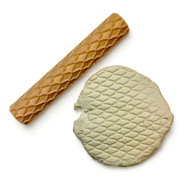 A seamless texture roller and flattened chunk of clay featuring a scallop diamond pattern are against a white background.