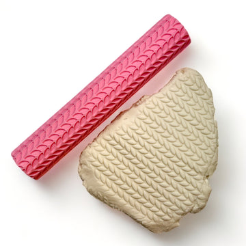 A seamless texture roller and flattened chunk of clay featuring a palm leaves pattern are against a white background.