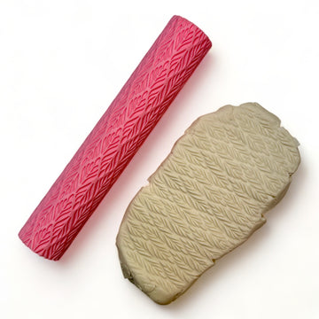 A seamless texture roller and flattened chunk of clay featuring a repeating leaf pattern are against a white background.