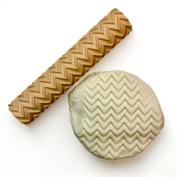 A seamless texture roller and flattened chunk of clay featuring a zig zag pattern are against a white background.