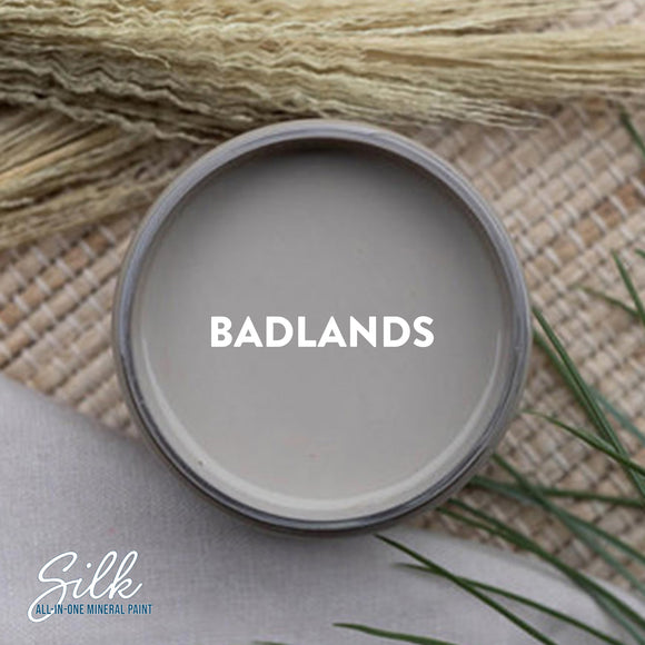 An arial view of an open container of Dixie Belle Paint Company's Badlands Silk All-In-One Mineral Paint is shown with white text reading Badlands