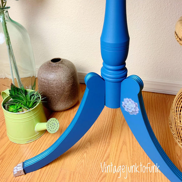 A close-up of a small side table's base refurbished by Vintage Junk to Funk features Dixie Belle's Cape Current Silk All-In-One Mineral Paint.