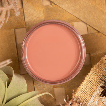 An arial view of an open container of Dixie Belle Paint Company's Desert Rose All-In-One Silk Paint is on a wood lattice table with burlap and light green foliage.