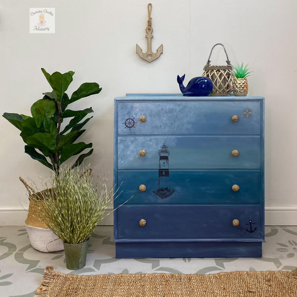 A 4-drawer chest dresser refurbished by Cherubs Chalks Interiors has an ocean inspired design that features Dixie Belle's Nautical ilk All-In-One Mineral Paint on the bottom drawer and base.