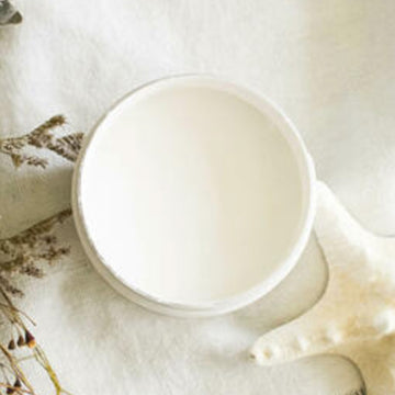 An arial view of an open container of Dixie Belle Paint Company's Salt Water All-In-One Silk Paint is on a white material with a bleached star fish and dried beach flowers.