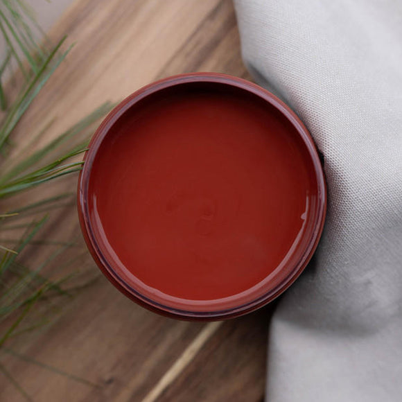 An arial view of an open container of Dixie Belle Paint Company's Sequoia All-In-One Silk Paint is on a wood table with a white cloth napkin and green grassy foliage.