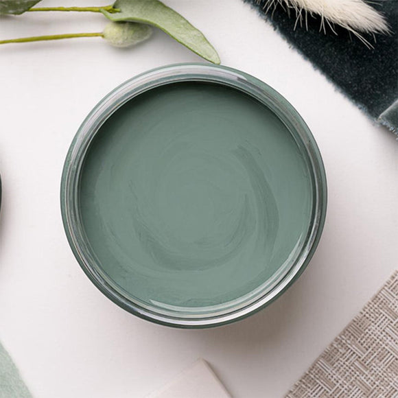 An arial view of an open container of Dixie Belle Paint Company's Blue Grass Chalk Mineral Paint is on a white table with other items.