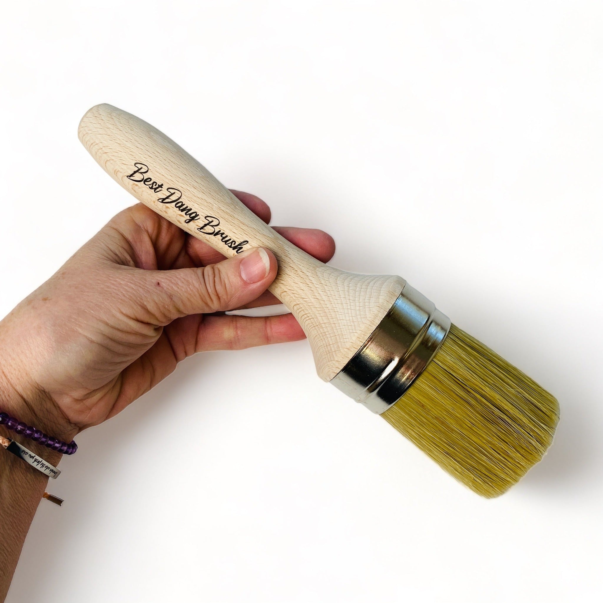 A hand holding Dixie Belle Paint's Best Dang Brush against a white background. This is a 2-inch natural blend that is excellent for painting, blending, and/or waxing.