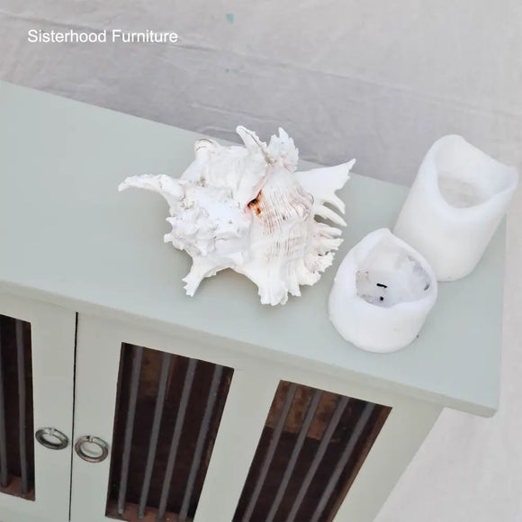 Decorative shell and candle holders on a light green surface with 'Sisterhood Furniture' branding.
