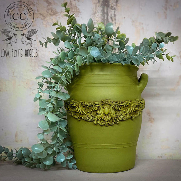 A ceramic vase refurbished by Low Flying Angels that resembles a milk can  features Dixie Belle's Everglades Silk All-In-One Mineral Paint with a decorative flourish silicone mold casting.