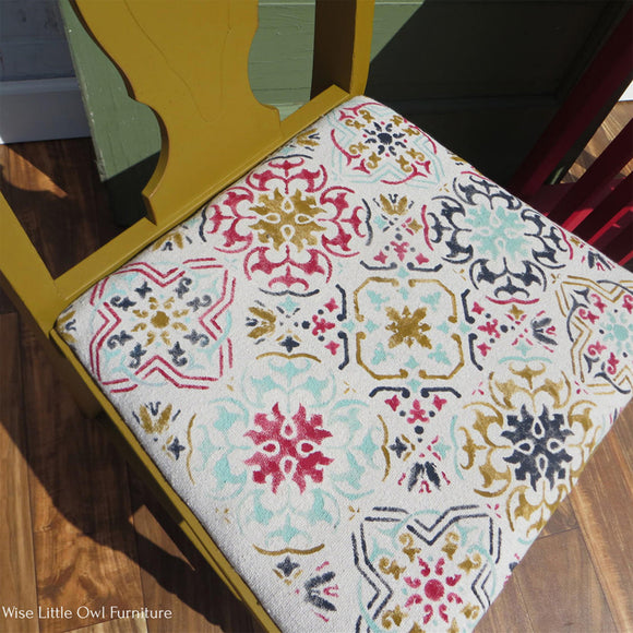 A vintage table chair refurbished by Wise Little Owl Furniture has a stencil design on its cushion seat that features Dixie Belle's Fiery Sky Silk All-In-One Mineral Paint along with a few other paint colors.