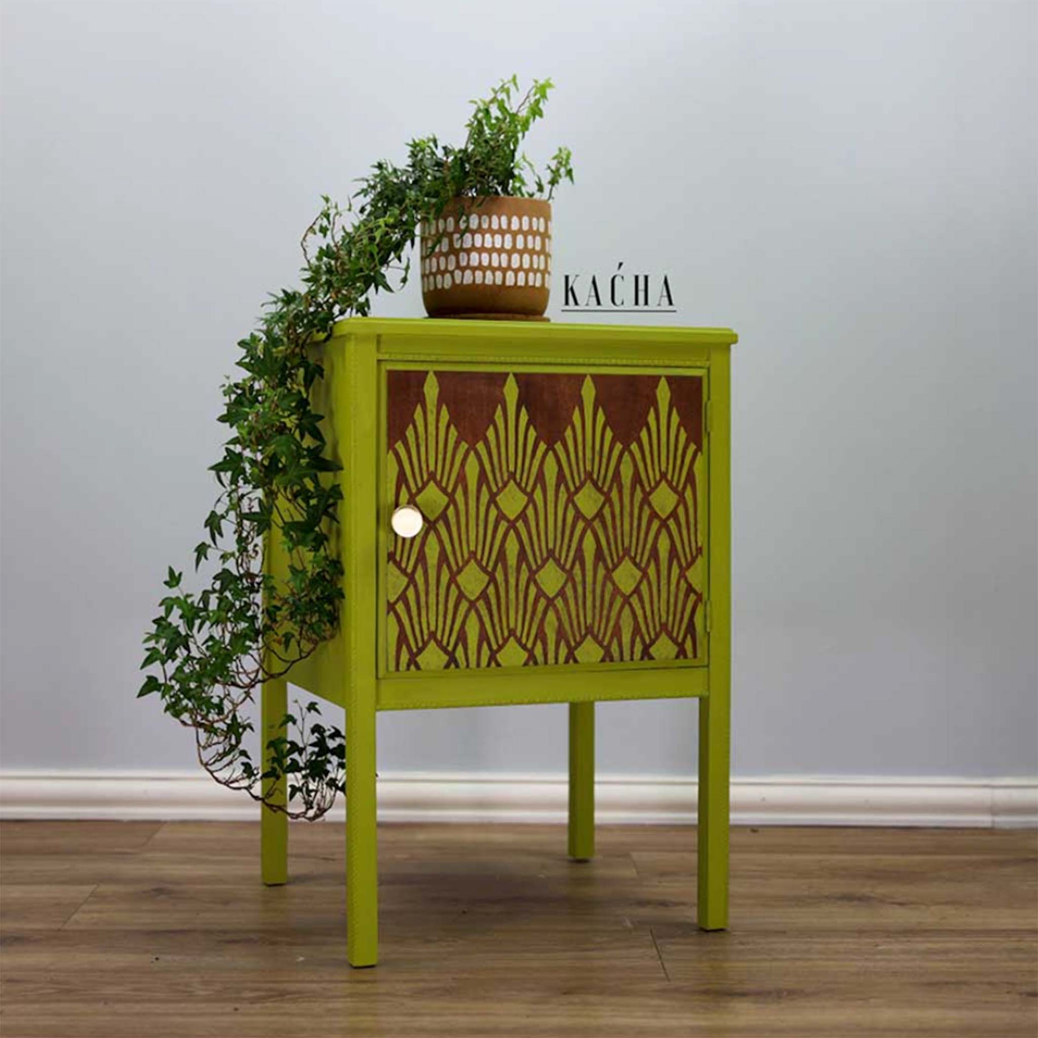 A small 1-door nightstand refurbished by Kacha is painted avocado green. The door is stained a dark wood color and features ReDesign with Prima's Sunlit Diamonds stencil in avocado green.