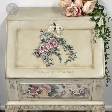 A vintage secretary's desk features ReDesign with Prima's Velvet Cascade Right decor poly applique on its lift-up lid and is painted soft pink and green.