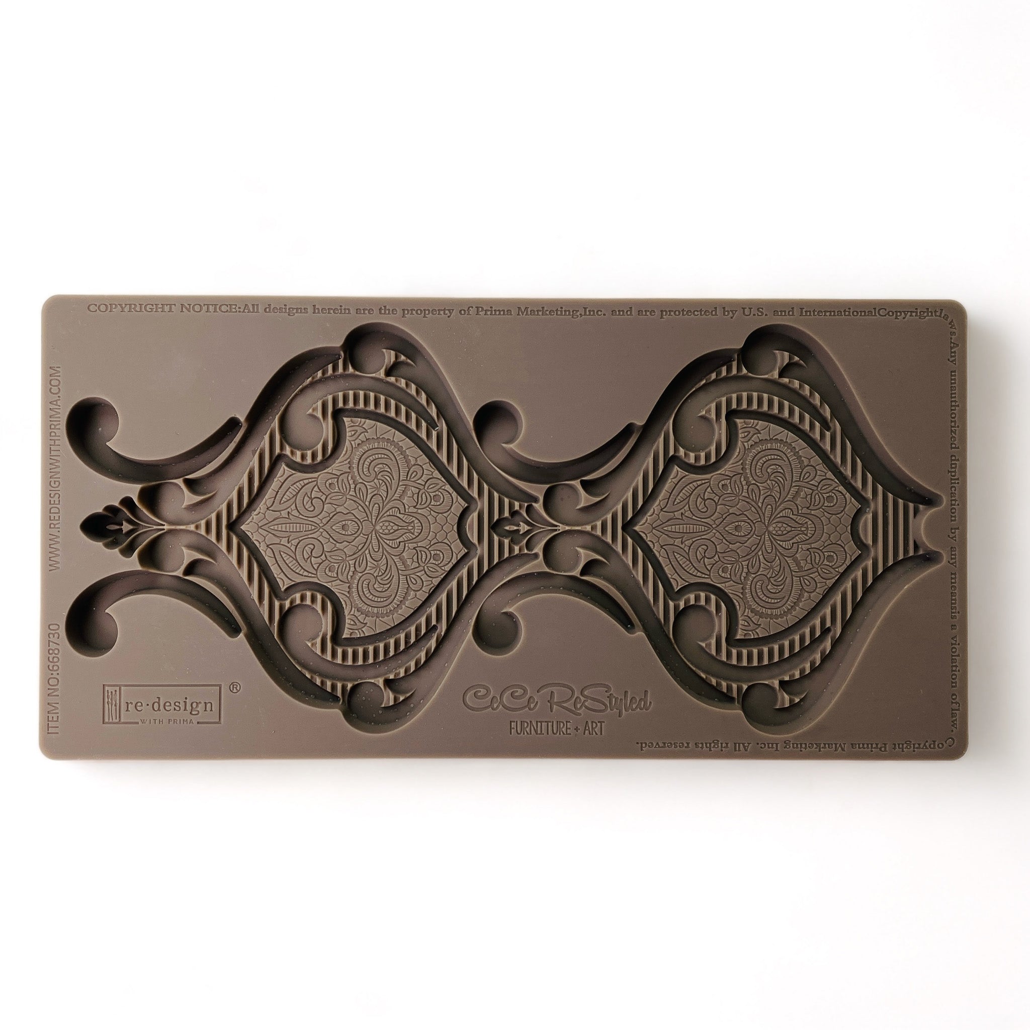 A brown silicone mold that features a large hourglass shaped medallion is against a white background.