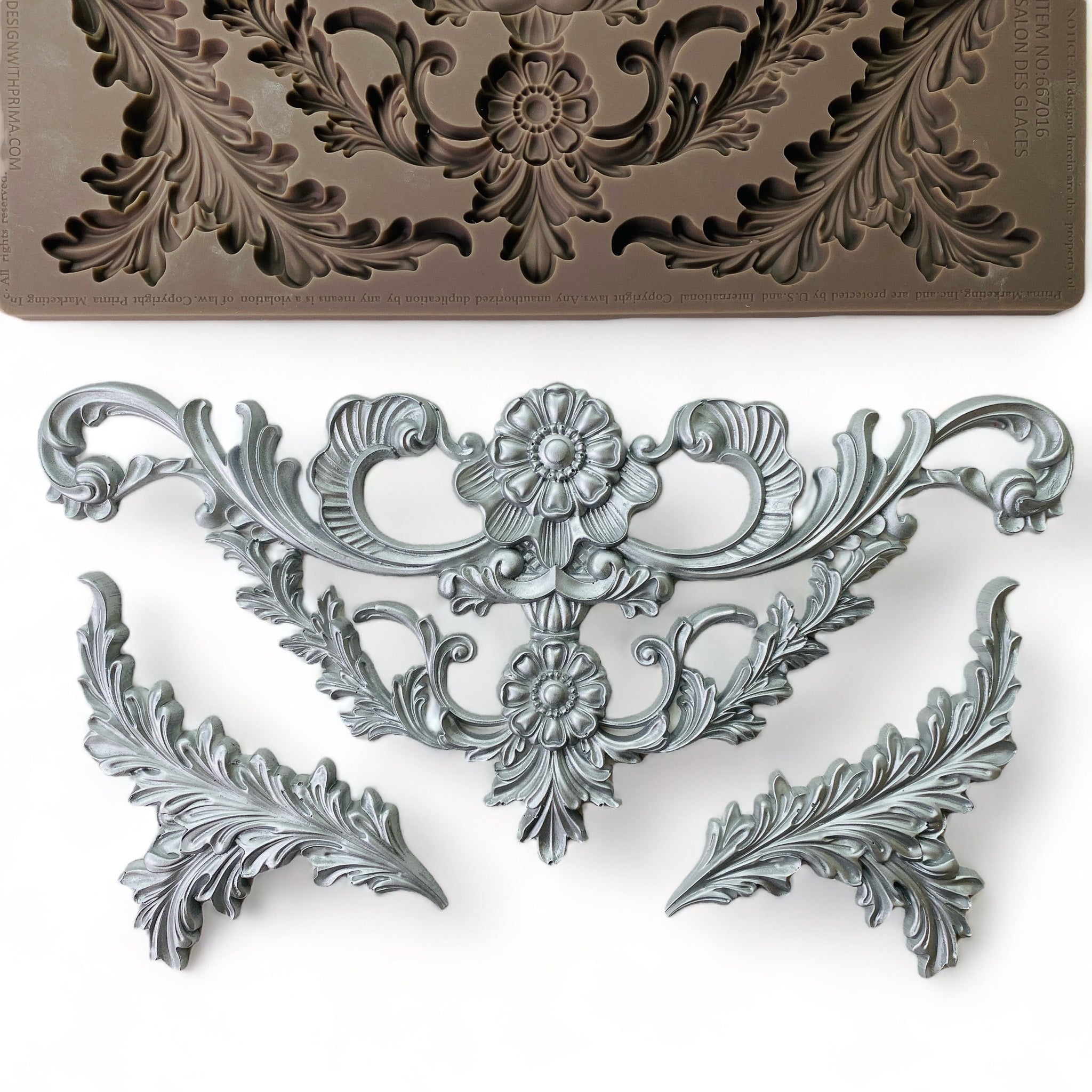 A brown silicone mold and silver-colored castings of a large ornate scroll floral leaf accent piece and 2 leaf plumes are against a white background.