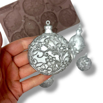 Decorative silver ornament held in a hand with a mold in the background