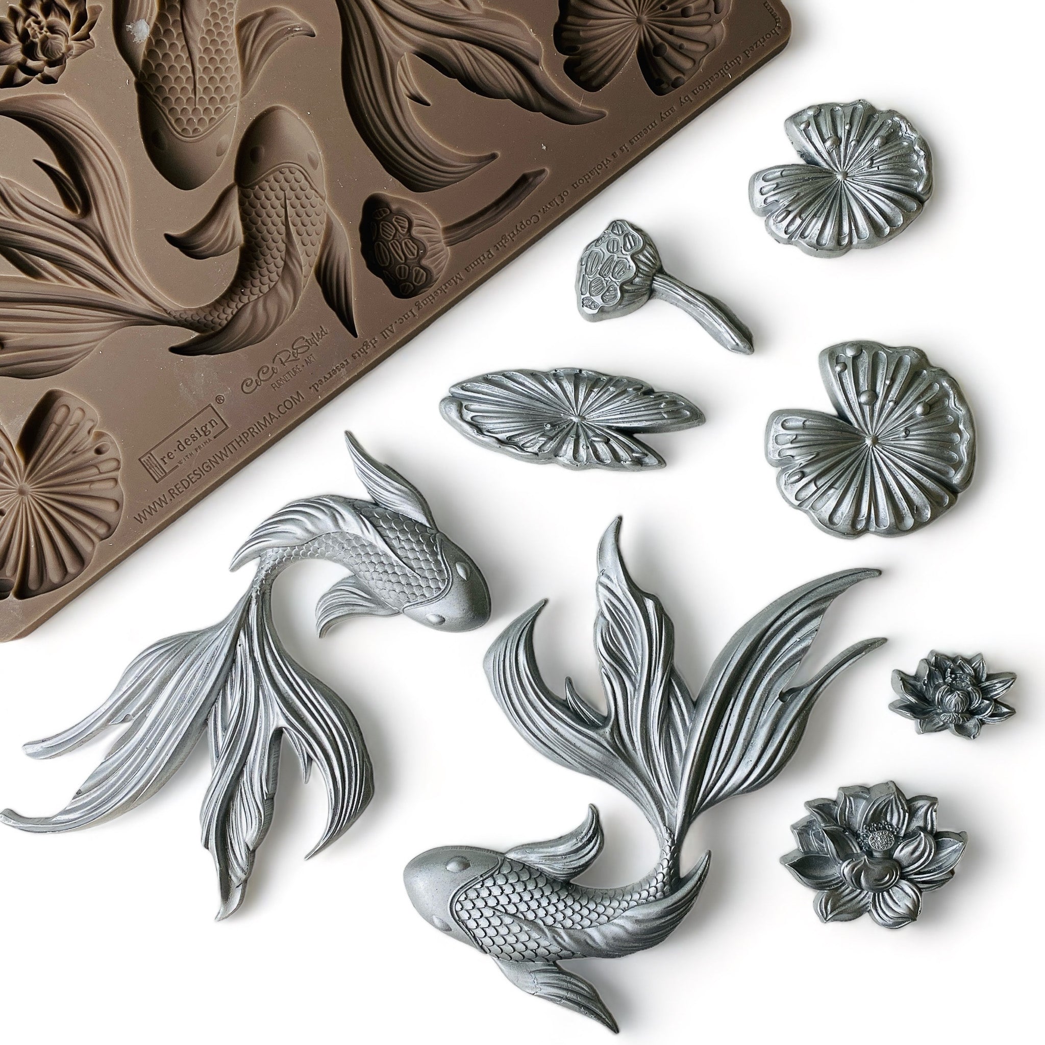 A brown silicone mold and silver-colored castings featuring 2 intricately-detailed koi fish, surrounded by water lilies and lily pads are against a white background.