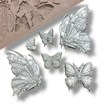 A silicone mold and silver colored castings featuring 6 intricate butterflies, each embellished with cogs and gears are against a white background.