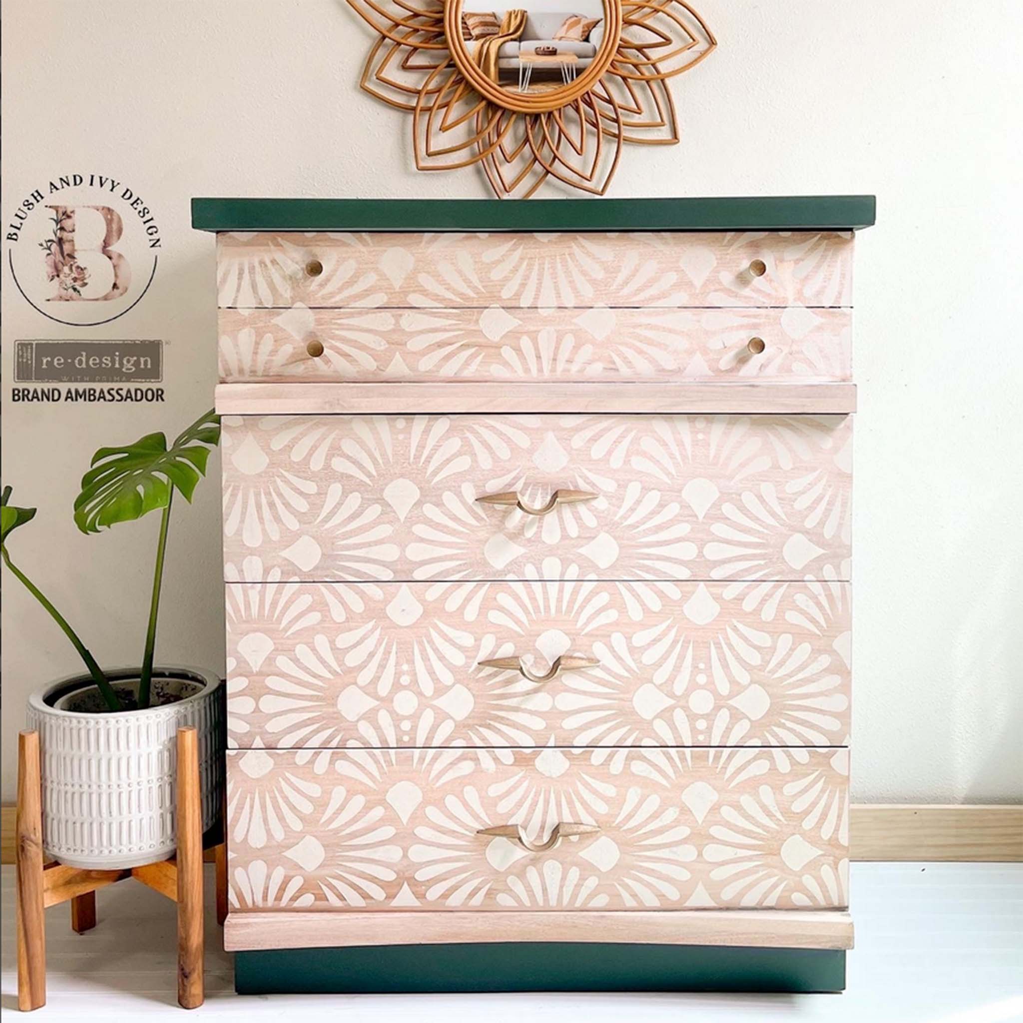A vintage 5-drawer chest dresser refurbished by Blush & Ivy Design is a natural light wood with dark green on the top and bottom panels. ReDesign with Prima's Modern Deco stencil is in white against the natural wood drawers.