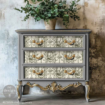 A vintage 3-drawer chest dresser is painted grey with gold accents and features ReDesign with Prima's KACHA Chasing Petals fiber paper on the drawers.