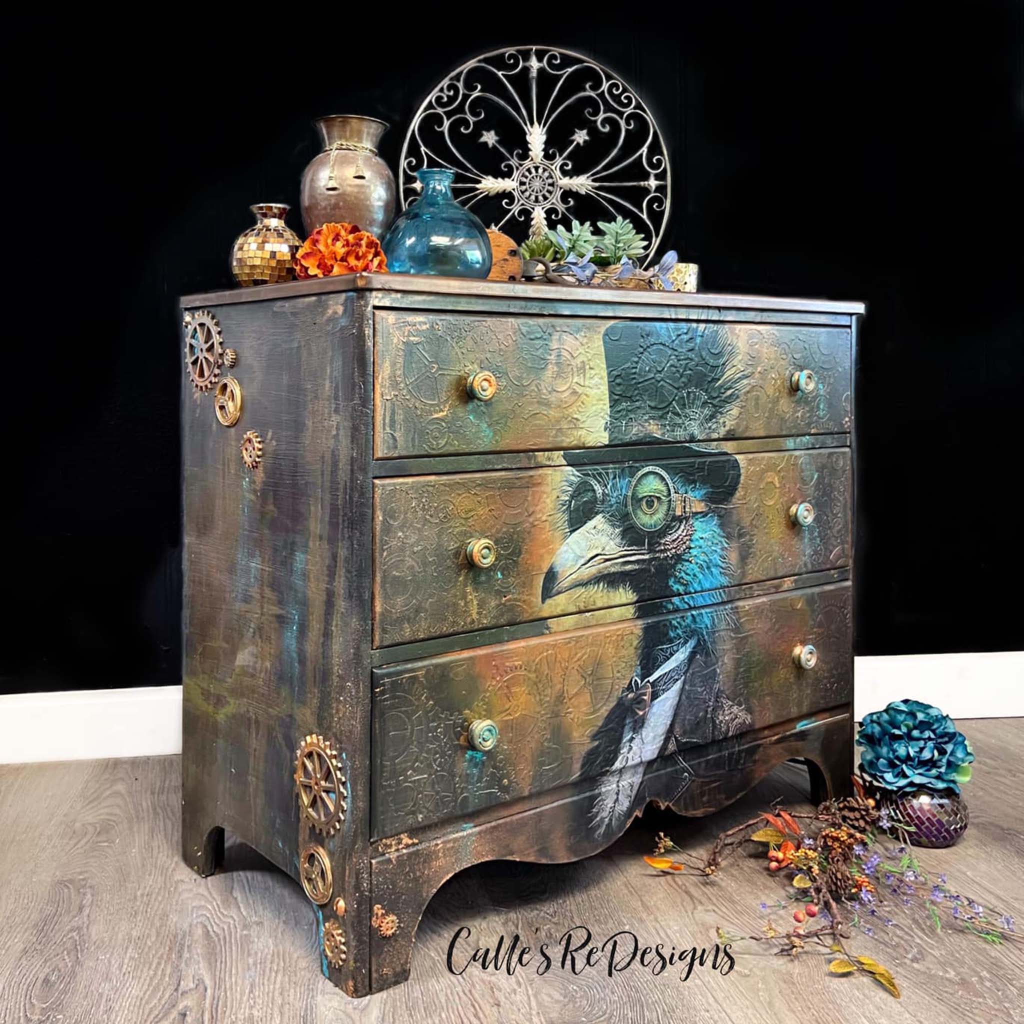 A vintage dresser refurbished by Calle's ReDesigns is painted a blend of brown, blue, and orange to create a rust look and features Whimsykel's Cogsworth tissue paper on the entire front.