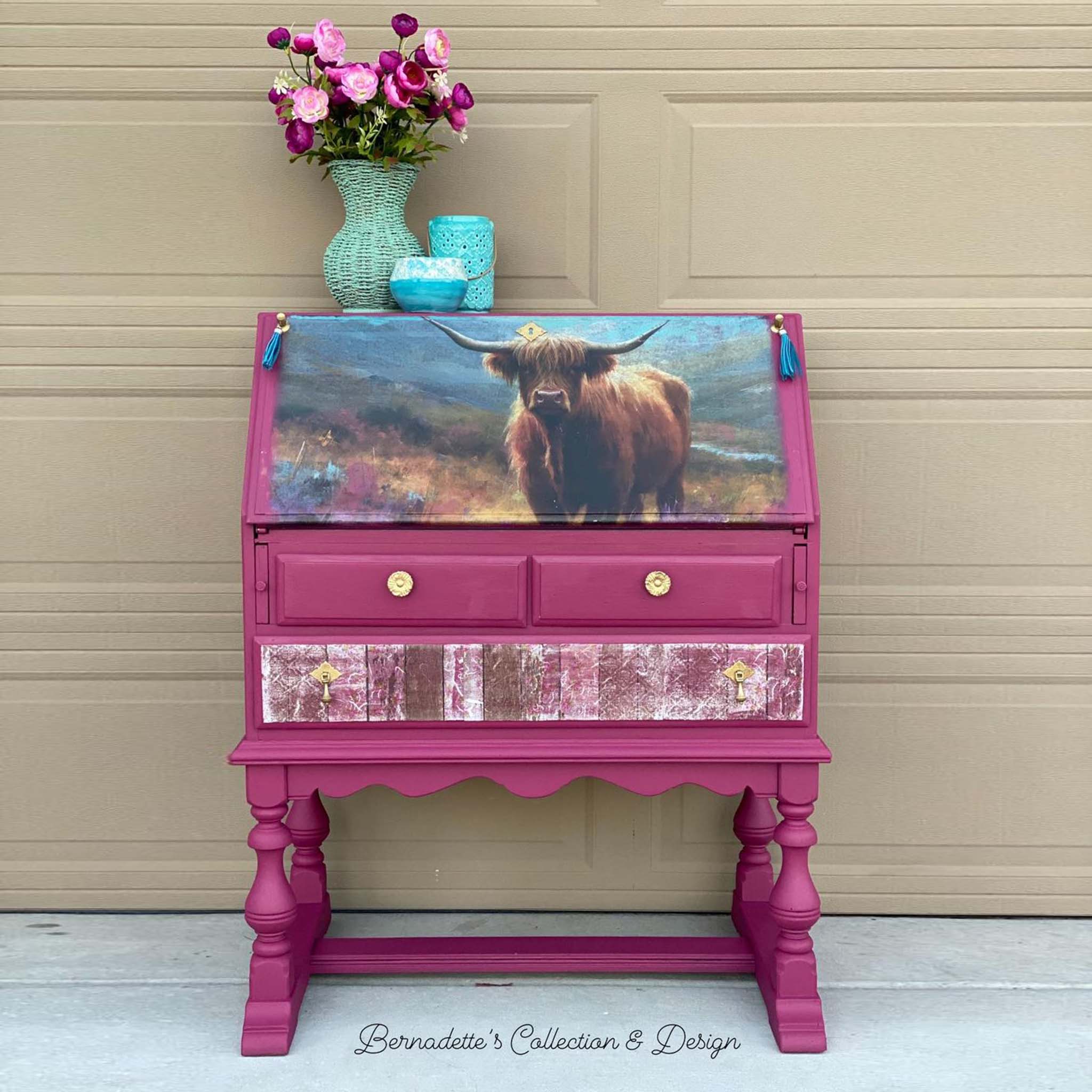 A vintage secretary desk refurbished by Bernadette's Collection & Design is painted a mid-dark pink and features Whimsykel's Flora Highland Cow tissue paper on its drop down door.