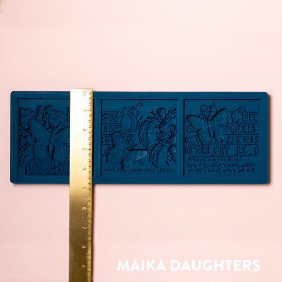 A blue silicone mold of 3 tiles featuring butterflies, flowers and calligraphy is against a light pink background. A gold ruler reading 4.8" height sits on the mold.