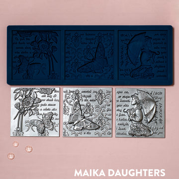 A blue silicone mold and silver colored castings of 3 tiles featuring a woman holding an umbrella, butterflies, flowers, and script writing are against a light pink background.