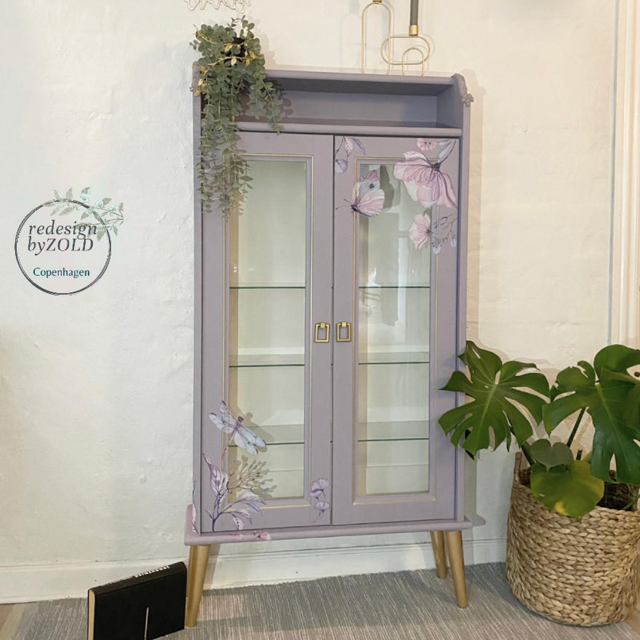 An enclosed bookcase refurbished by Redesign by Zold Copenhagen is painted a soft purple and features the Translucent Garden Transfer on the front.