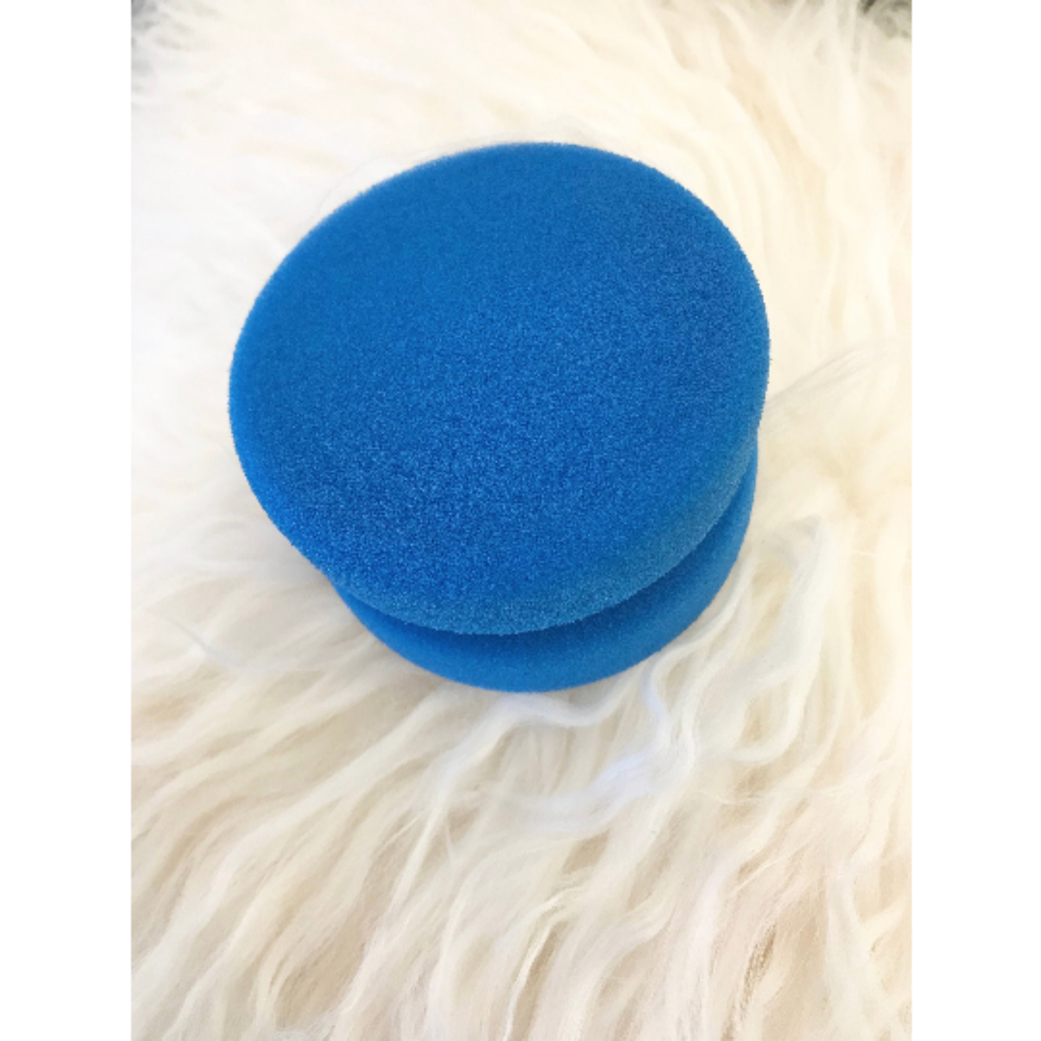 Dixie Belle Paint's Blue Sponge Applicator is against a white faux fur background. White borders are on the sides.