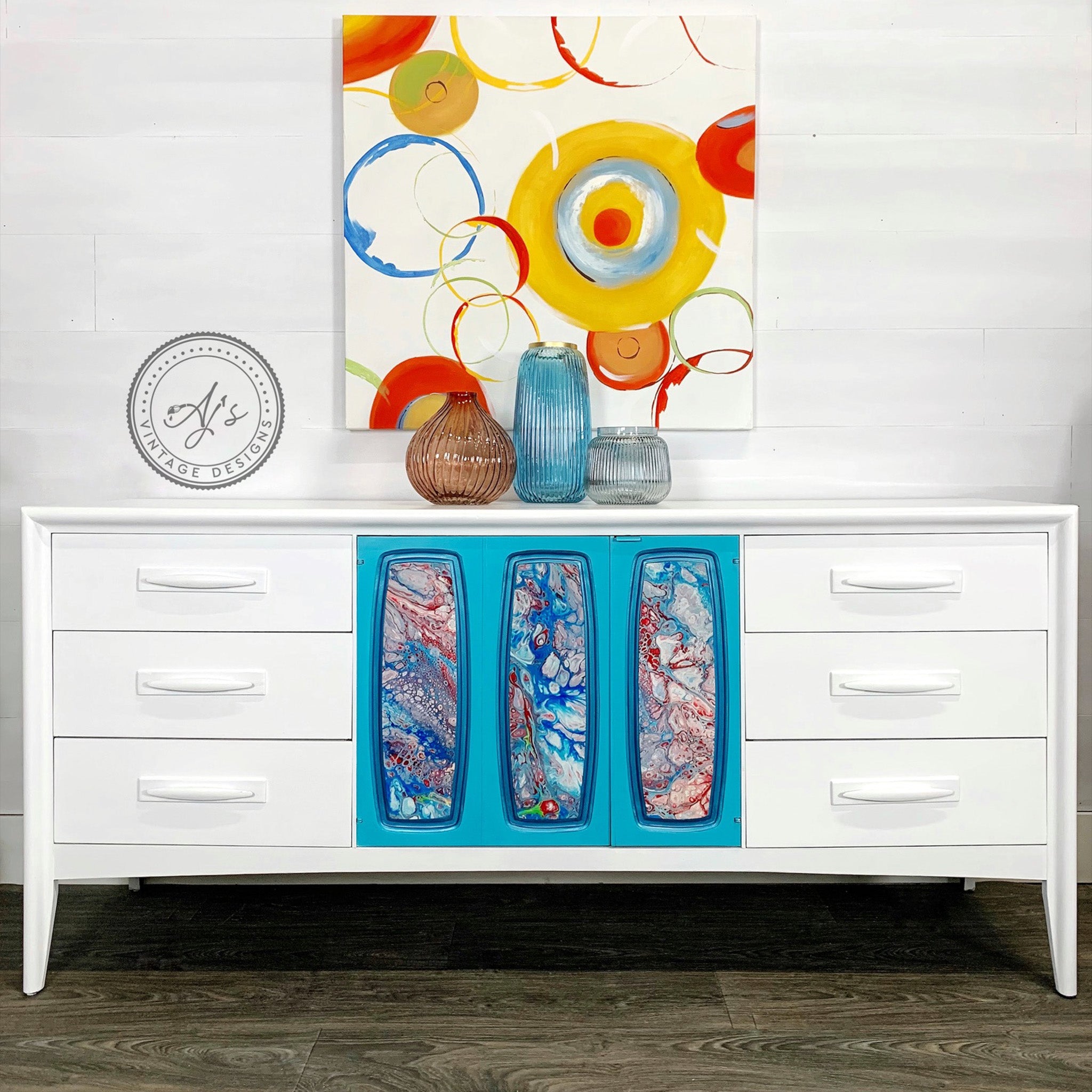 A vintage large dresser refurbished by Aj's Vintage Designs is painted in Dixie Belle's Cotton chalk mineral paint. The center of the dresser has a tri-fold door painted in sky blue with a blue and red marble design.