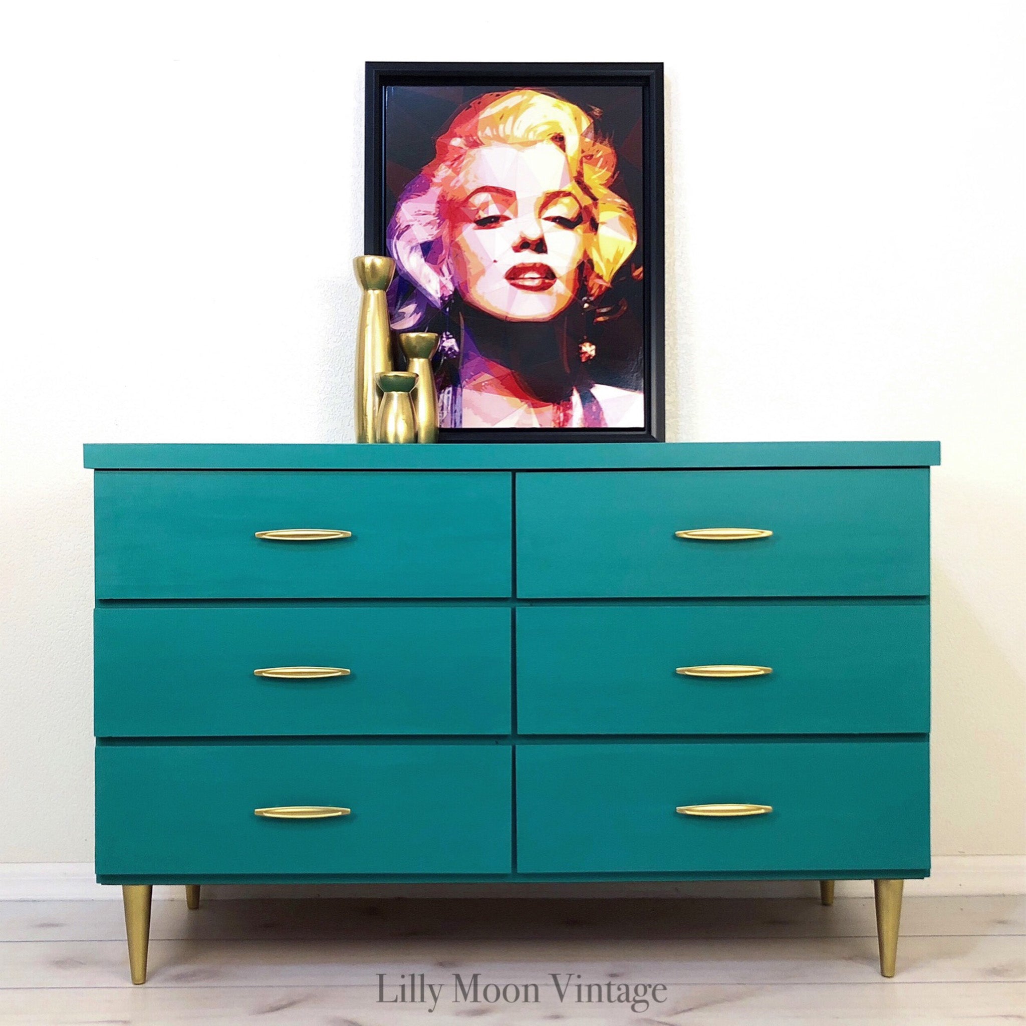 A mid-century dresser refurbished by Lilly Moon Vintage is painted in Dixie Belle's Mermaid Tale and has gold drawer pulls and legs.
