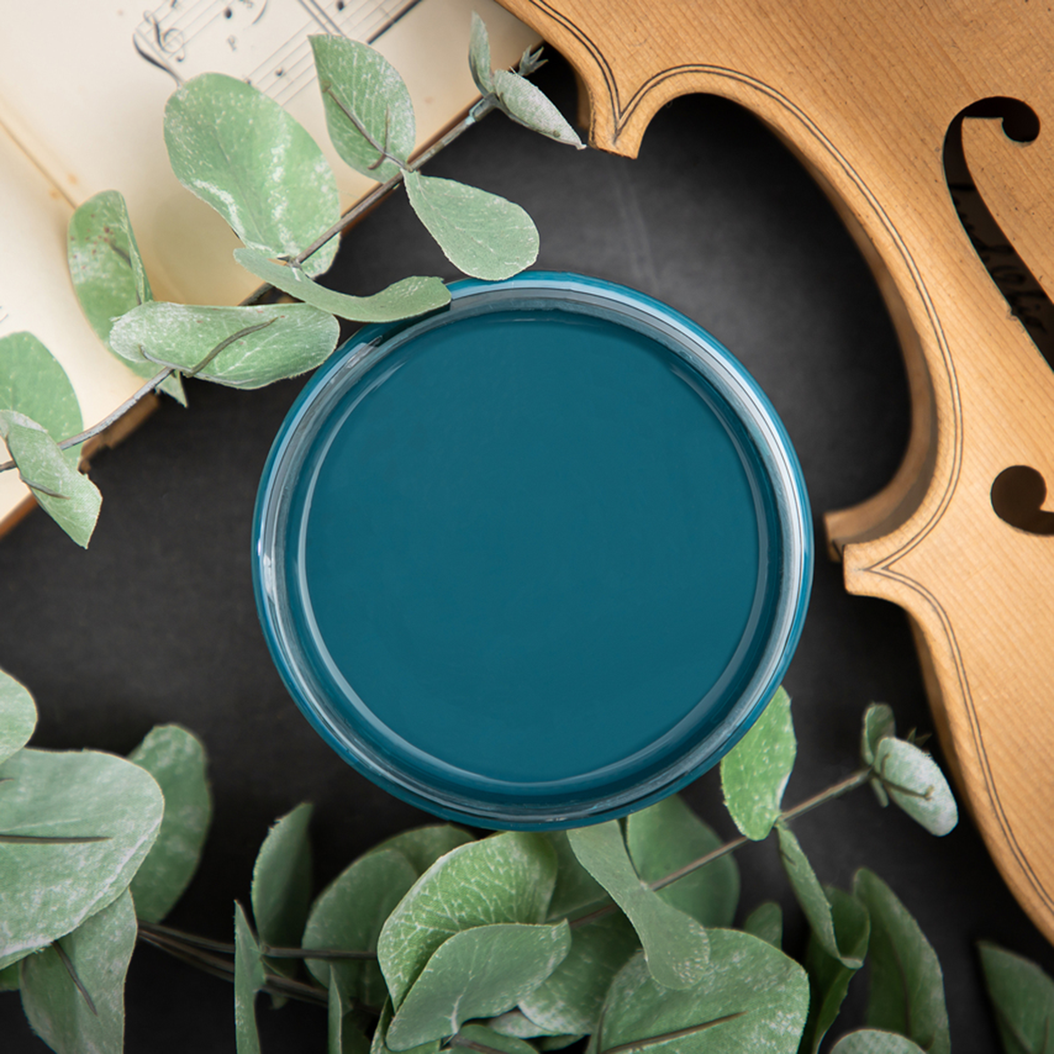 An arial view of an open container of Dixie Belle Paint Company's Antebellum Blue Chalk Mineral Paint surrounded by a violin and leaves.