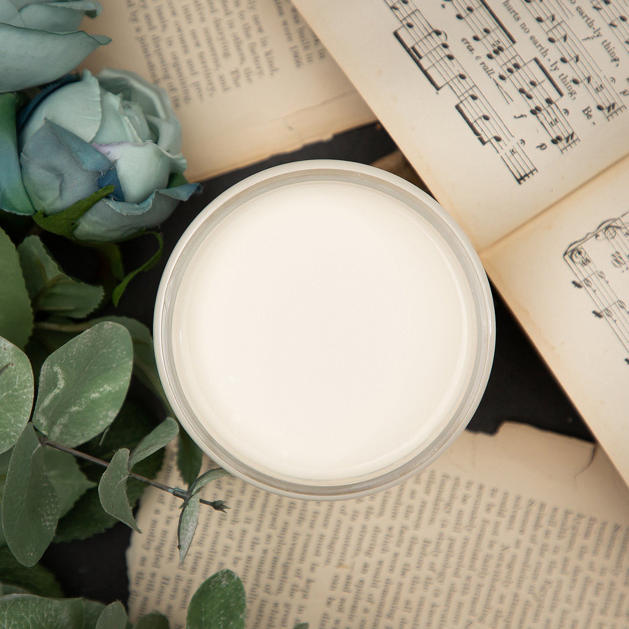 An arial view of an open container of Dixie Belle Paint Company's Buttercream Chalk Mineral Paint is surrounded by sheet music and flowers.