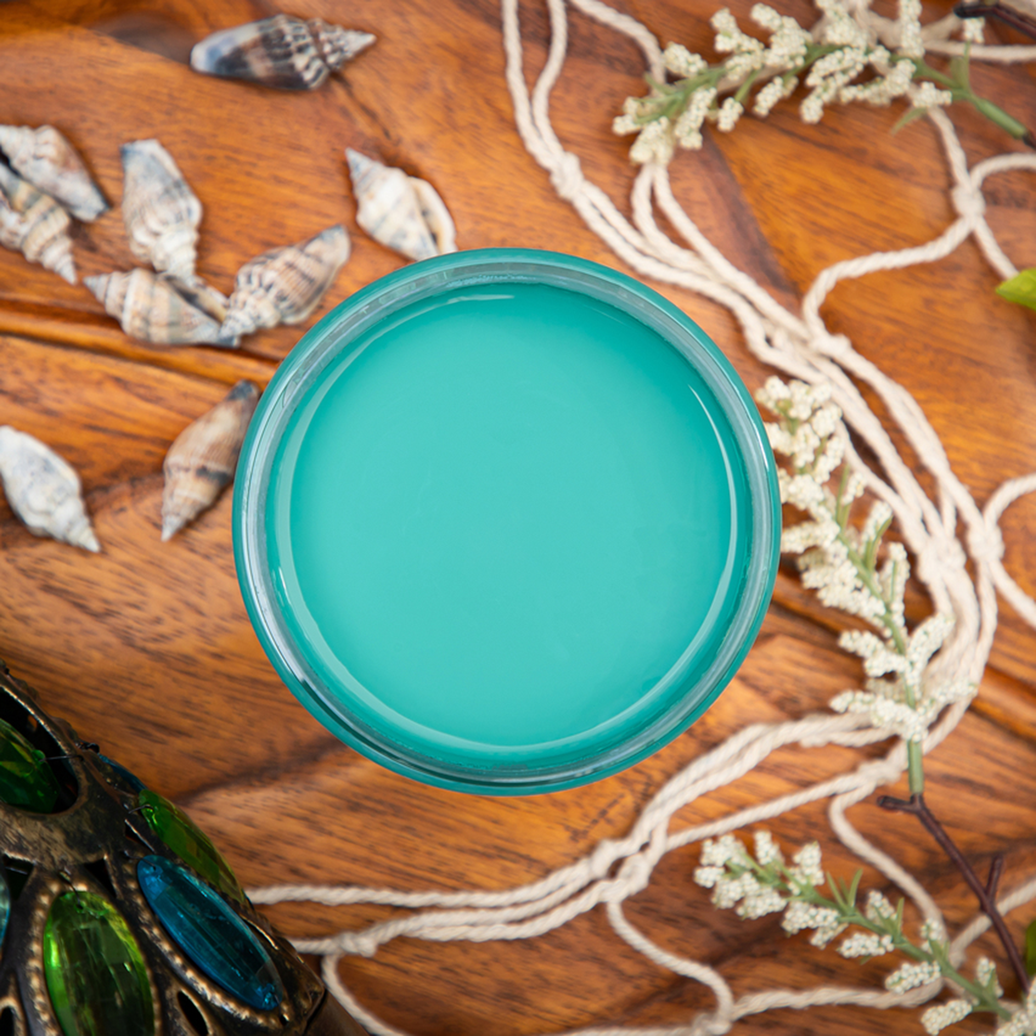 An arial view of an open container of Dixie Belle Paint Company’s Mermaid Tail Chalk Mineral Paint is on a wood table and surrounded by sea shells and rope